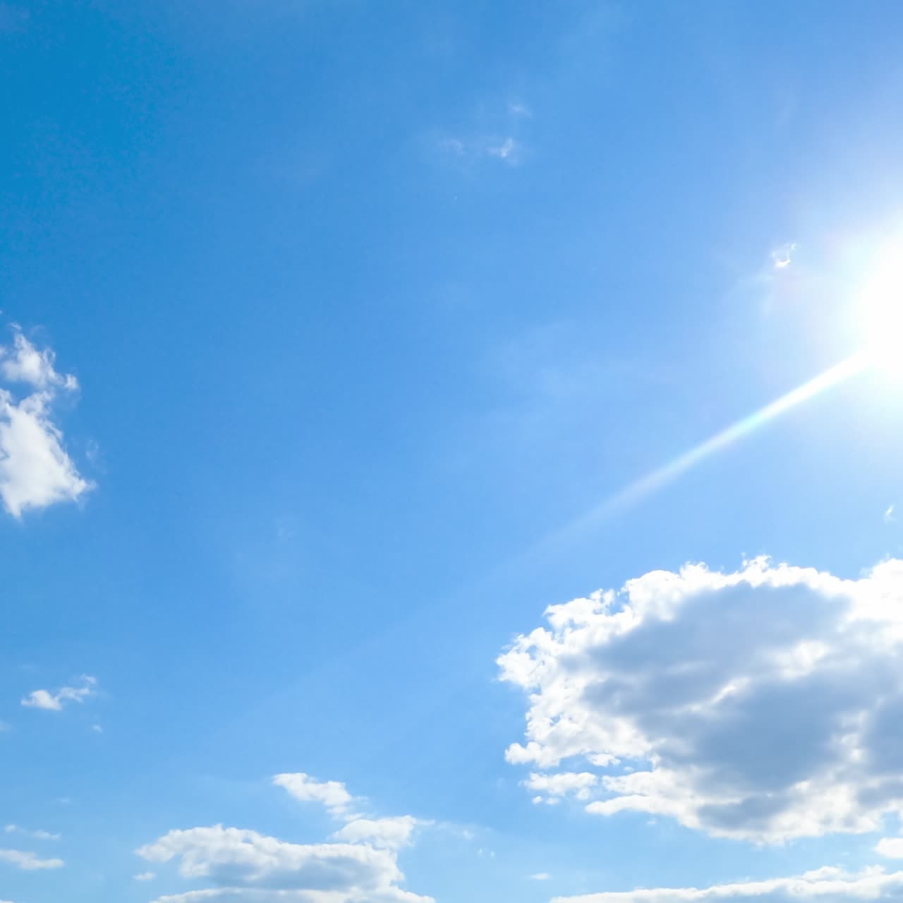 Clear blue sky with brightly shining sun. Light white clouds accumulating and covering the sun for moment. Timelapse