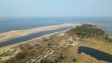 Drone-flies-over-Mikoszewskie-lake-and-Vistula-River-of-Mewia-Lacha-Nature-Reserve-during-a-sunny-day,-Baltic-Sea-in-background