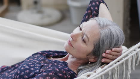 Caucasian-middle-aged-woman-relaxing-in-hammock-on-terrace-in-nature,-slow-motion