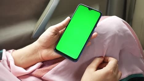 woman holding a smartphone with a green screen in a car