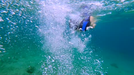 Mujer-Con-Aletas-Buceando-En-Agua-De-Mar-Tropical-Turquesa-Haciendo-Burbujas-De-Oxígeno,-Tiro-Bajo-El-Agua-En-Cámara-Lenta