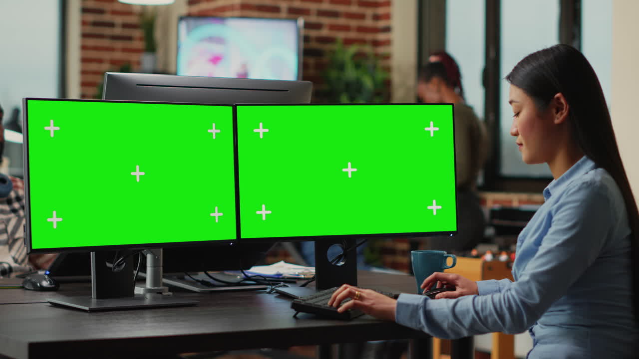 Asian freelancer looking at greenscreen on multi monitors