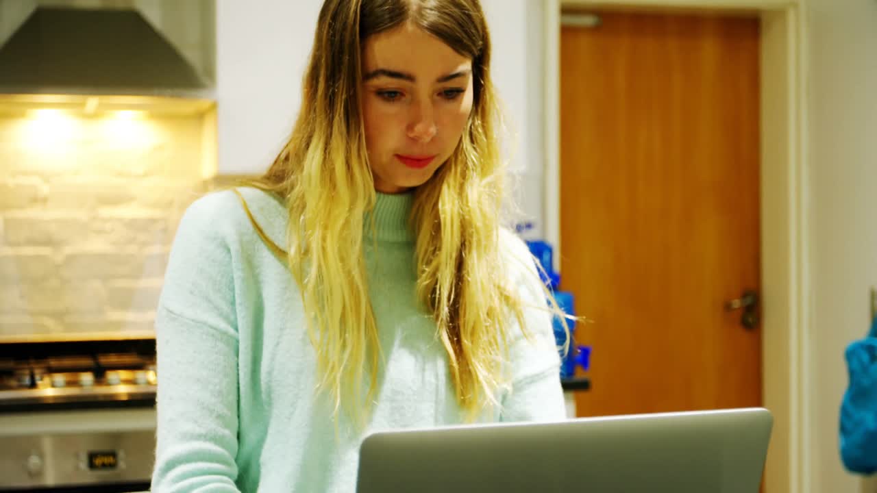 mujer tomando café mientras usa portátil en la cocina 4k