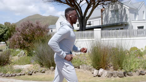 Focused-african-american-man-jogging-with-headphones-on-street-on-sunny-day,-slow-motion