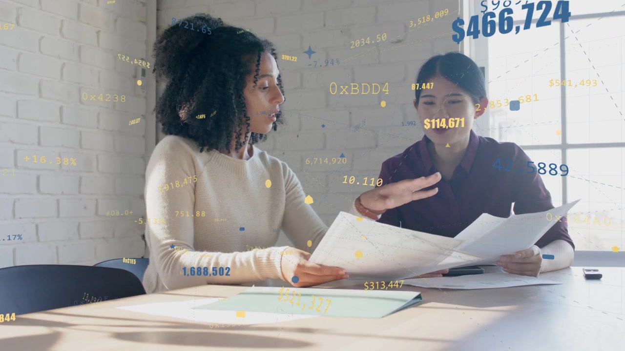 Two women working swapping pages and pointing turning pages with animated finance numbers floating
