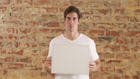 caucasian man holding a white rectangle on a brick wall