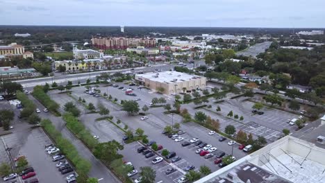 forward moving aerial drone shot of shopping mall parking lot with buildings in foreground and busy road with interesection in background