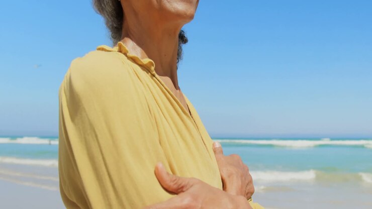 Side view of happy active senior African American woman with arms crossed standing on the beach 4k