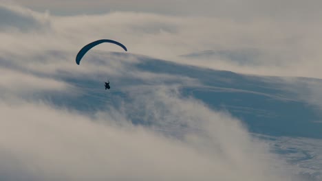 Paraglider-shot-against-the-light-with-snow-covered-hills-and-clouds-in-the-background,-Cumbria-UK