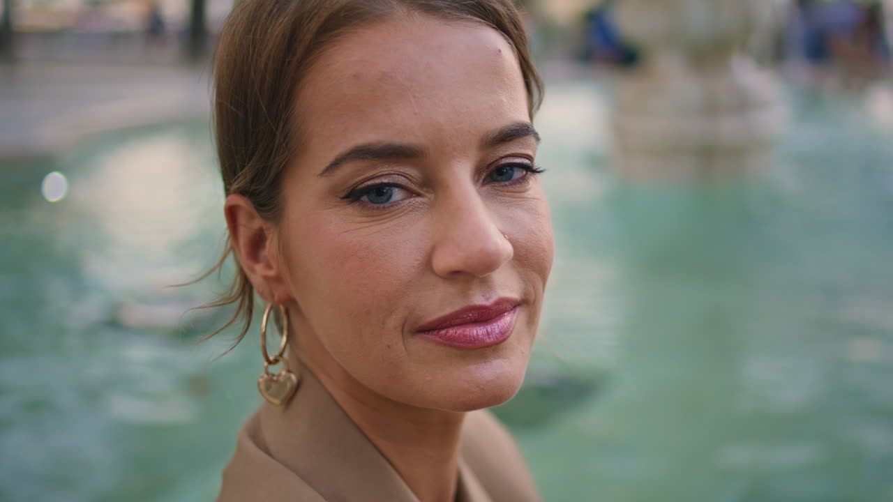 Senhora elegante olhando para a câmera em close-up perto de uma fonte de água. Mulher atraente ajustando o cabelo.