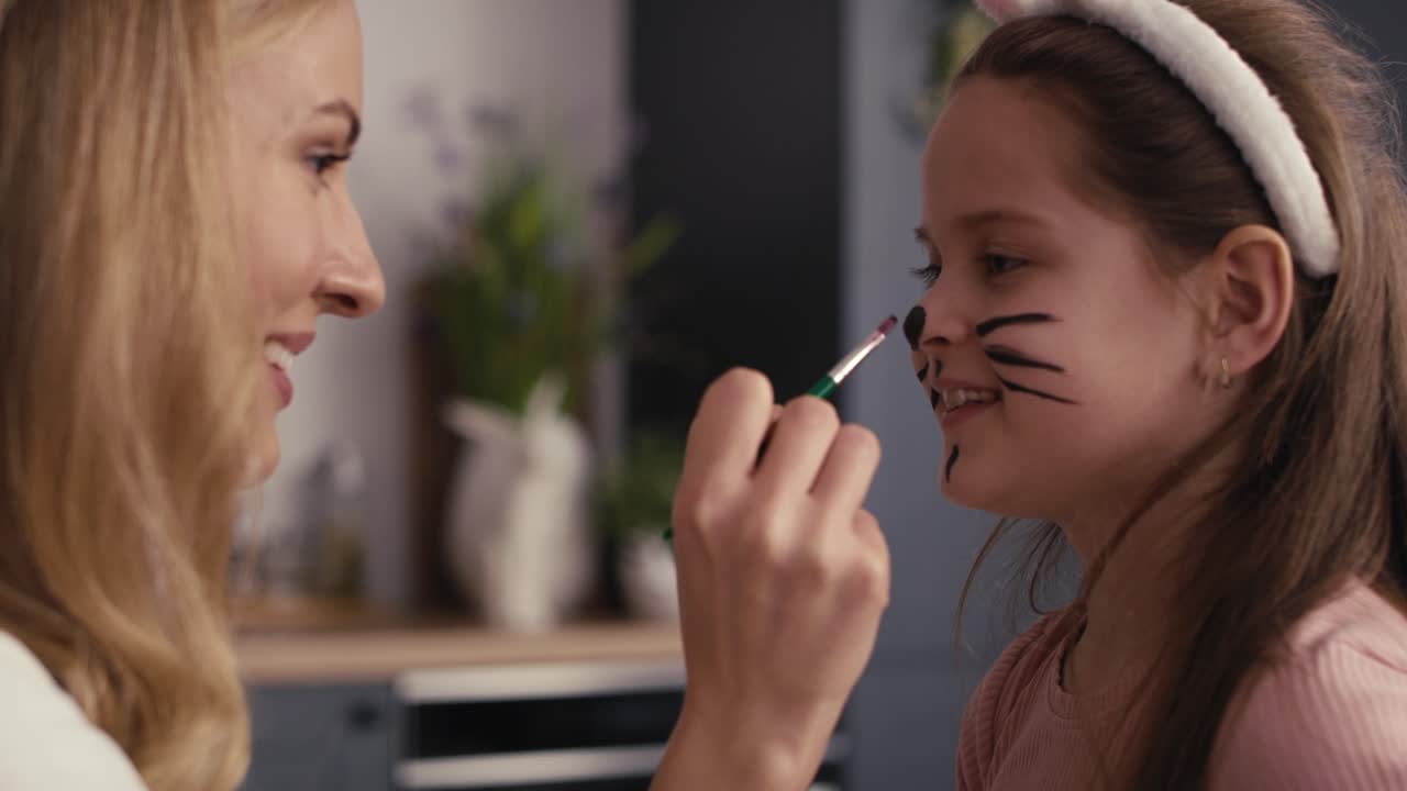 Side view of caucasian mother and daughter painting easter bunny on girl's face.