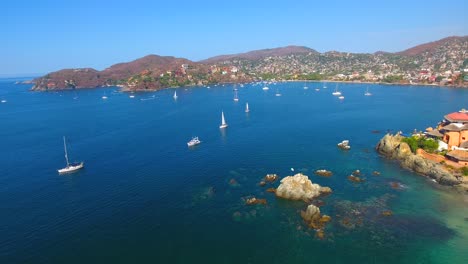 stationary aerial view of a busy ocean bay filled with sailboats and yachts off the coast of zihuatanejo, mexico