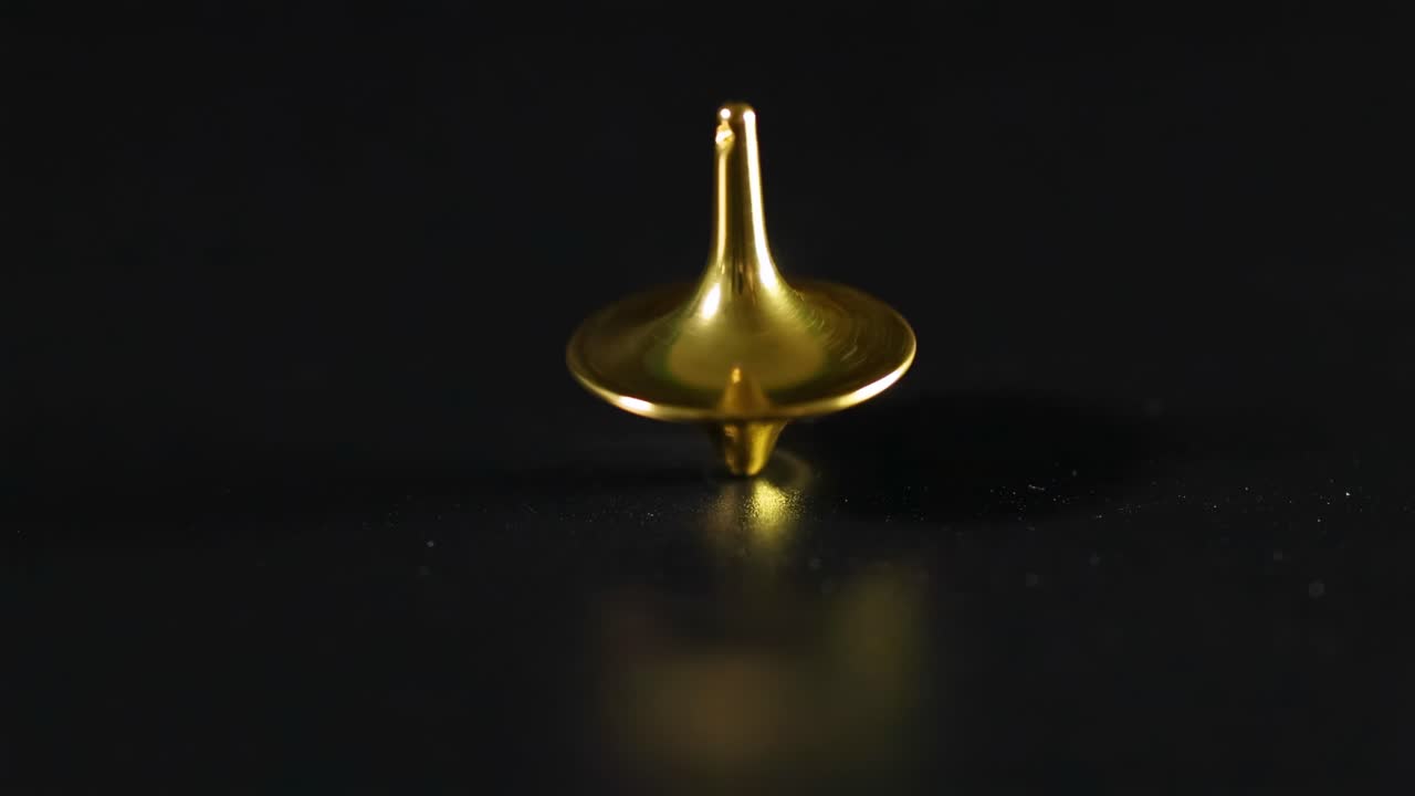 A golden top spins steadily on a dark surface, showcasing its reflective metallic sheen.
