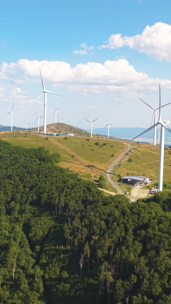 Shot from below in vertical format, wind turbine blades sweep through the sky with clouds adding depth and dimension