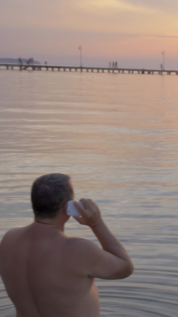 Man talking on phone in the sea at sunset