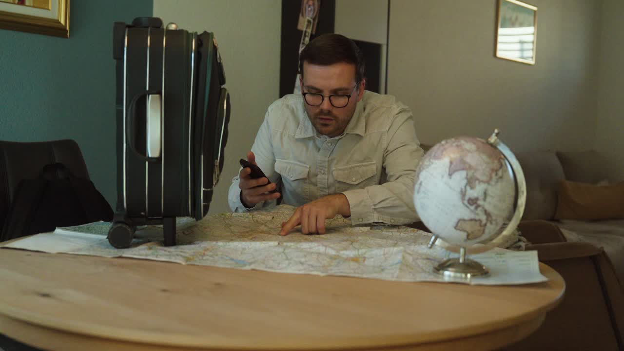 A man sits at a table with a vintage map while using an AI-powered smartphone app to plan his upcoming journey, blending modern technology with traditional travel methods