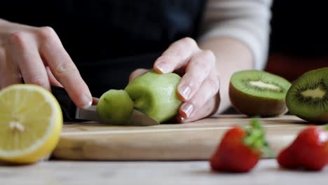 slowmotion of a woman cutting up fresh kiwis into slices with fruits laing around