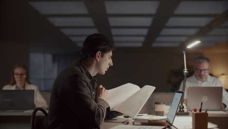 man working on laptop and reviewing documents during evening in office