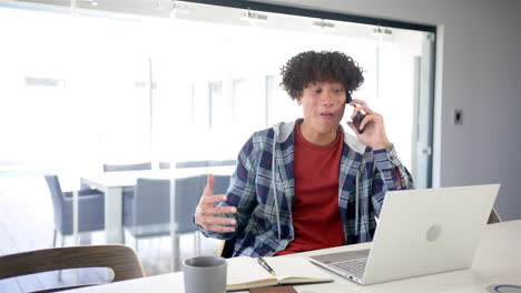 un joven biracial está en una llamada telefónica, usando una computadora portátil con espacio de copia