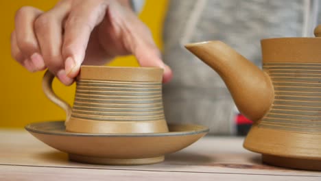 person hand holding tea cup over tea plate near teapot