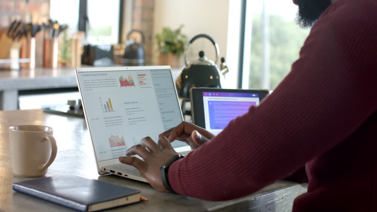 Upon hands landing on keys, man tapping and swiping to analyze charts on laptop in kitchen