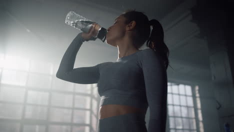 sportswoman drinking water in gym. girl taking rest after fitness workout