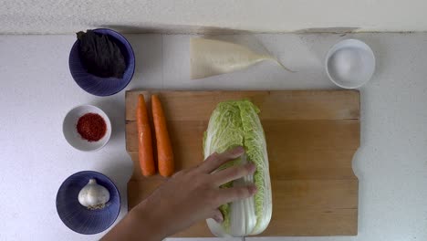 male hands cutting and tearing apart cabbage for kimchi on wooden cutting board