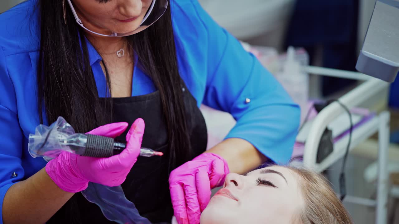 Tattoo on lips. Beautician doing permanent makeup on woman's lips. Young female getting permanent make-up on lips in a beauty salon.