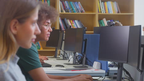 Estudiante-Universitario-O-Universitario-Masculino-Que-Trabaja-En-Una-Computadora-En-La-Biblioteca-Siendo-Ayudado-Por-Un-Tutor