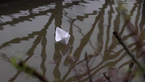 Papierboot-Schwimmt-Auf-Der-Wasserpfütze-Mit-Spiegelung-Des-Metallzauns