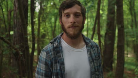 young caucasian male look up straight to the camera standing in a natural forest with tree on the background