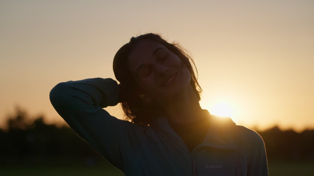 A person standing with their hand on their head, silhouetted against a sunset