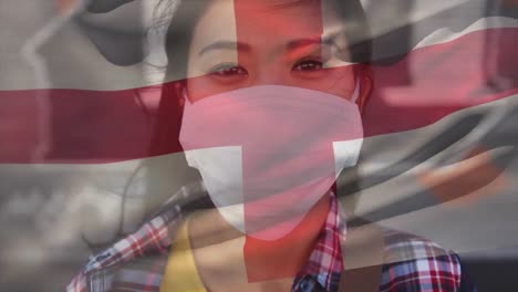 animation of flag of england waving over woman wearing face mask during covid 19 pandemic