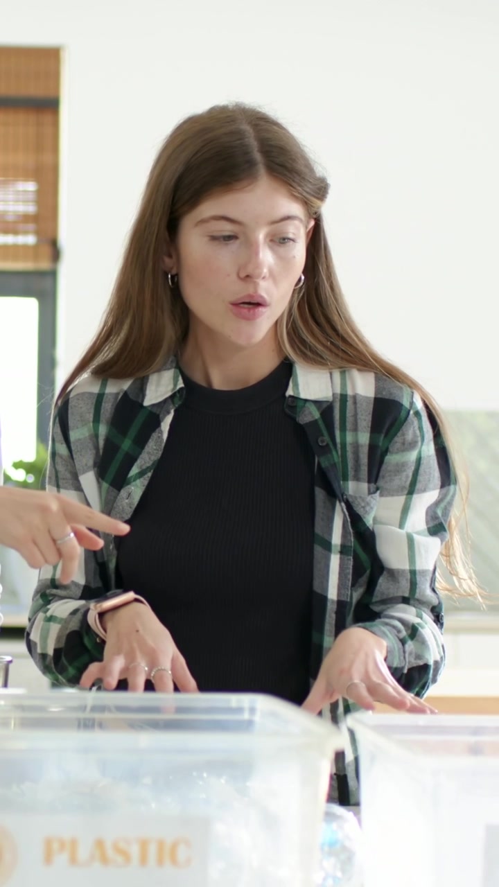 Video verticale: Donna che si gira, smista in contenitori di PLASTICA in cucina con un'amica in tuta gialla.