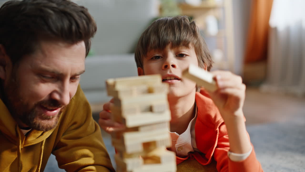 Primo piano di figlio che costruisce una torre di Jenga mettendo un blocco di legno in cima con il padre felice.