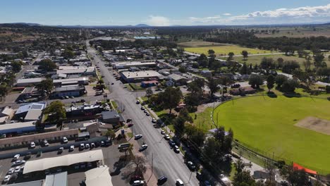 drone footage glides above a small australian town, showcasing busy streets, parked cars, and a large green park under bright daylight