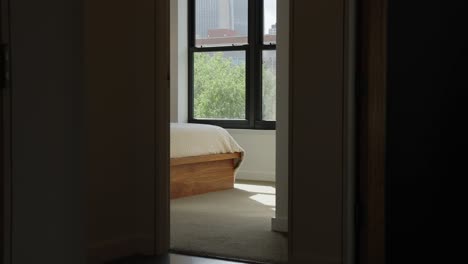 the corner of a bed from outside the room in the hallway with a window in the background