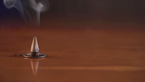 cono de incienso sentado sobre una superficie marrón cálida quemando y fumando