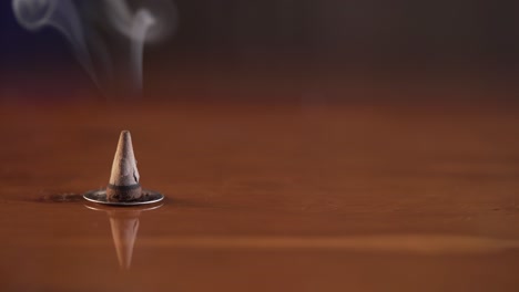 incense cone sitting on a warming brown surface burning and smoking