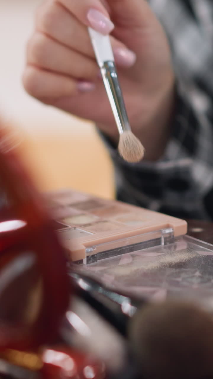 closeup brush dipping into palette, soft bristles lifting neutral shimmer from pans, manicured fingers guiding tool over compact, busy vanity foreground with brushes and case, studio camera setup