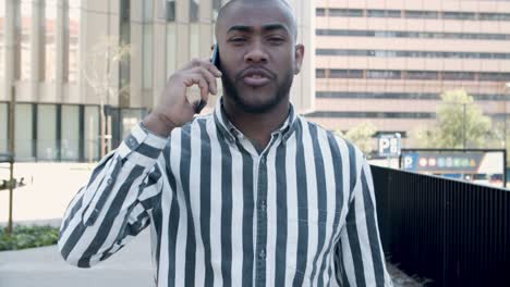 front view of serious young man talking on phone during stroll