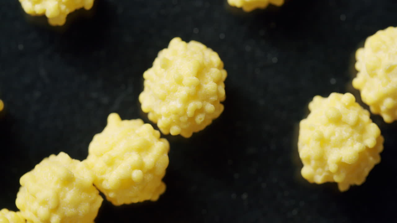 Macro top shot of yellow cells moving on a black surface. Surface spinning clockwise. Virus cells moving through the frame