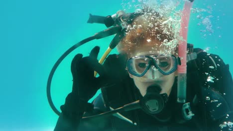 woman in scuba gear looking at camera underwater making ok sign