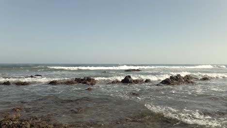 Aerial-Pan-View-of-Mediterranean-Sea-with-Waves-Splashing-on-Beach-Rocks,-Spain