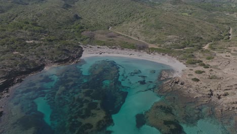 Panorámica-Aérea-De-La-Orilla-De-La-Bahía-Del-Océano-Azul-En-Cala-Sa-Torreta-Vegetación-Salvaje-Paisaje-Húmedo-De-Cala-Sa-Torreta-Menorca-España