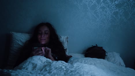 mujer sonríe a su teléfono mientras se desplaza a través de las redes sociales tarde en la noche