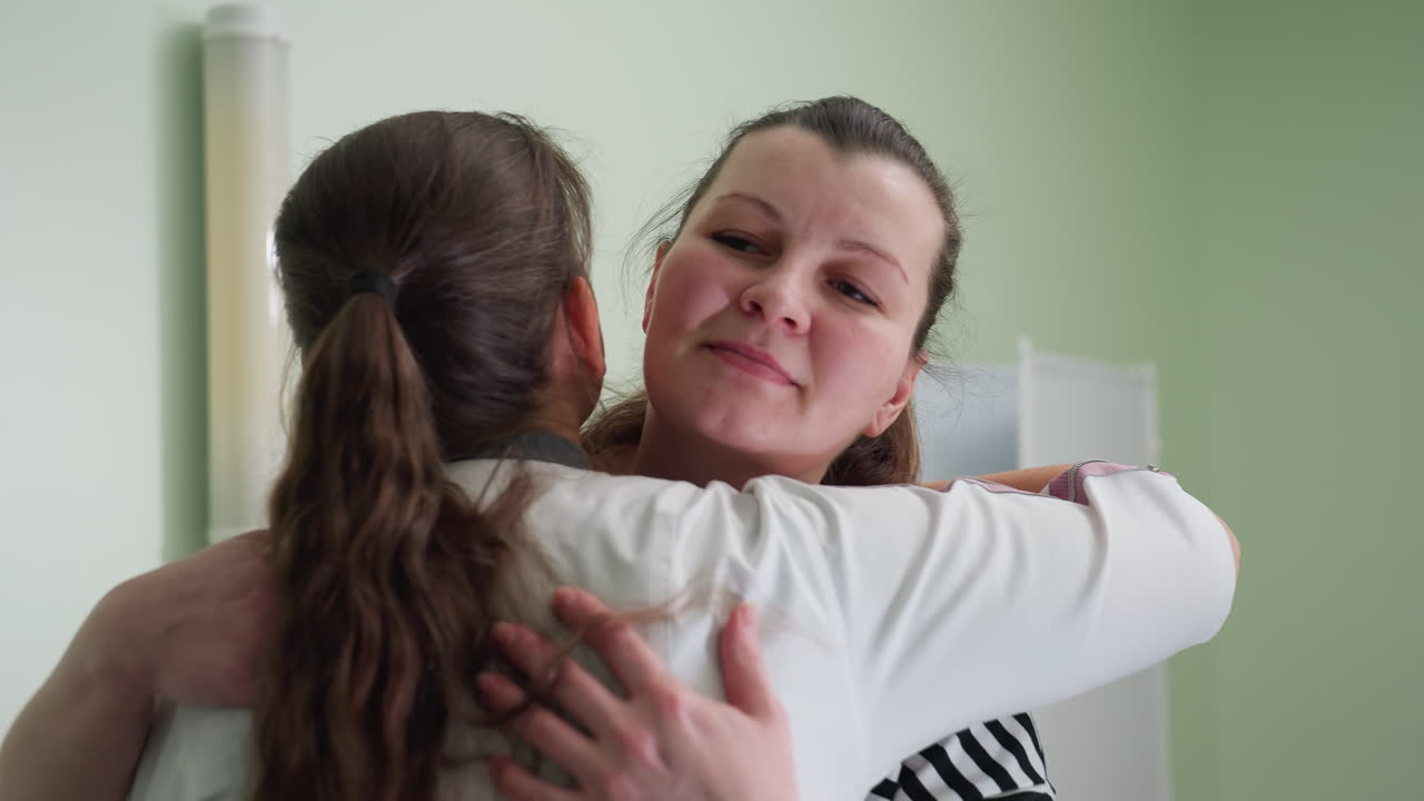 Woman approaches nurse inside clinic room and receives warm comforting hug with relief visible on her face conveying emotional support and trust in medical care during personal health consultation