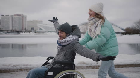 happy woman running with her disabled friend in wheelchair and having fun together in the city in winter