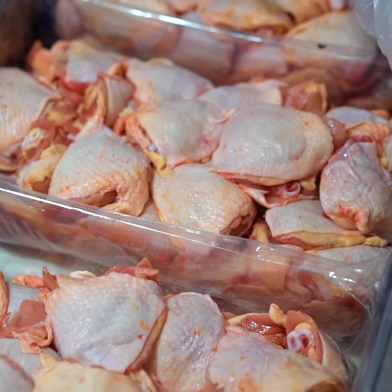 Fresh chicken products in refrigerator in a food farm. Appetizing chicken semi-finished products are on display in special containers. Worker laying out raw meat parts