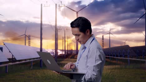 side view of an asian male professional worker standing with his laptop with solar panel and wind turbines, typing on his laptop's keybaord with meditation